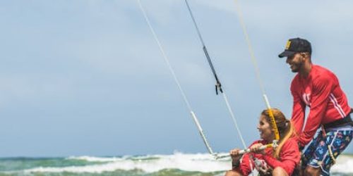 Instructor teaching kitesurfing to a student on a sunny beach day.